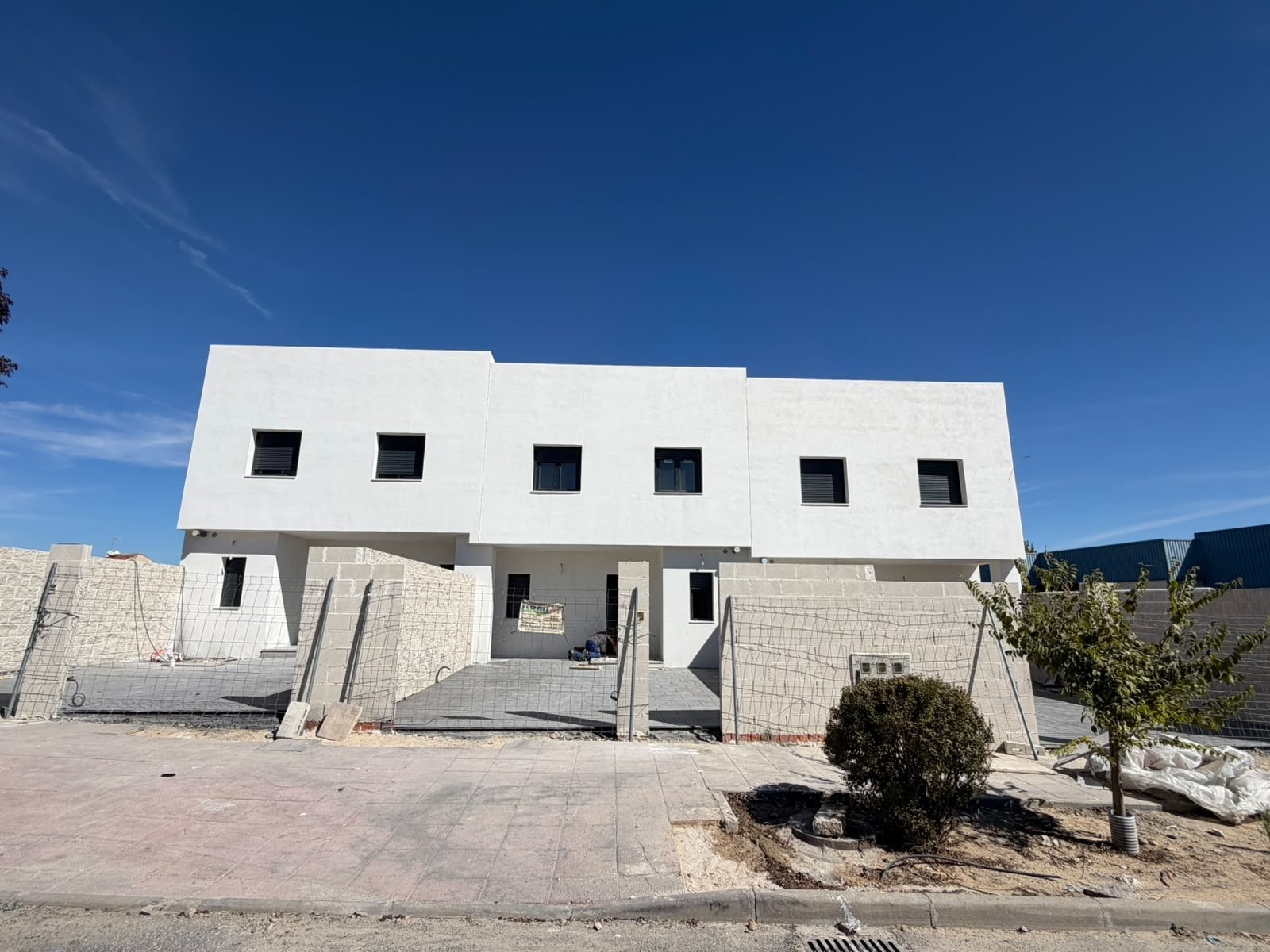 Vivienda adosada de obra nueva en construcción con fachada blanca, cubierta en pendiente y seis ventanales oscuros bajo un cielo azul