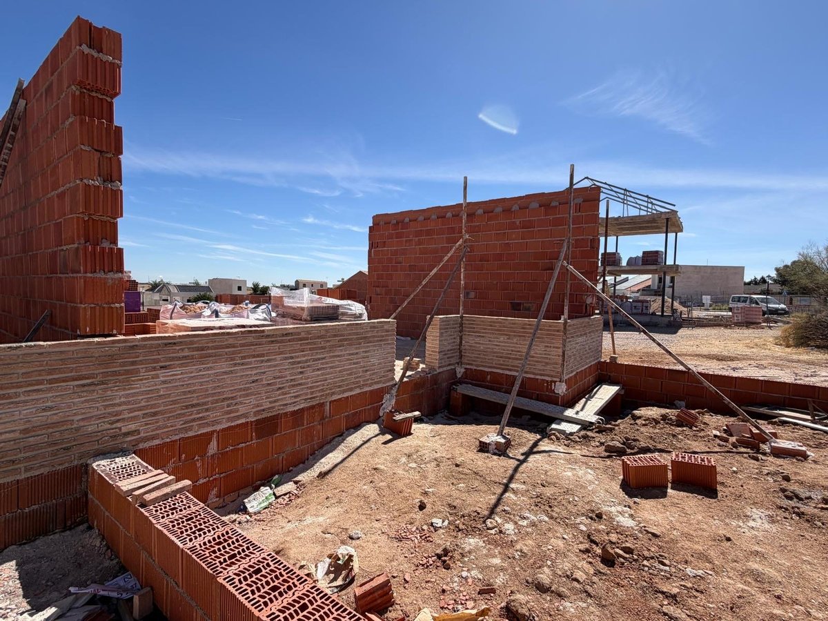 Detalle de la obra de los chalets adosados en Valmojado con muros de ladrillo, jácenas y material auxiliar de obra bajo cielo azul