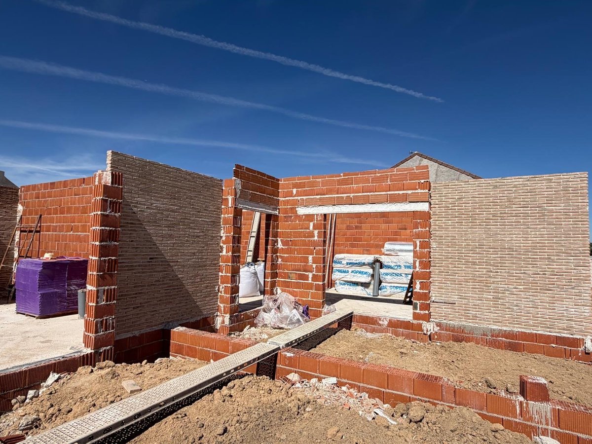 Bloque de viviendas en construcción en Valmojado con fábrica de ladrillo visto y aperturas de futuras ventanas bajo cielo azul