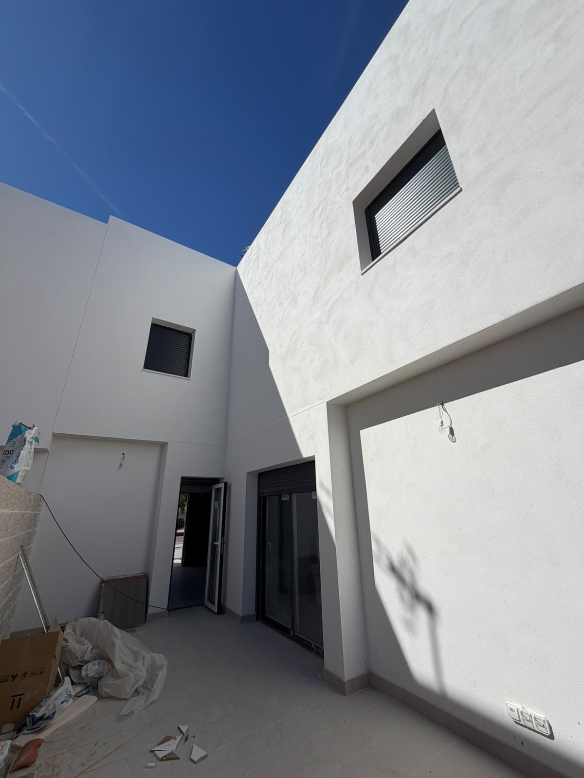 Patio interior de uno de los chalets adosados de Grama Homes con paredes blancas, puertas y carpintería en negro y suelo de gres bajo un cielo azul