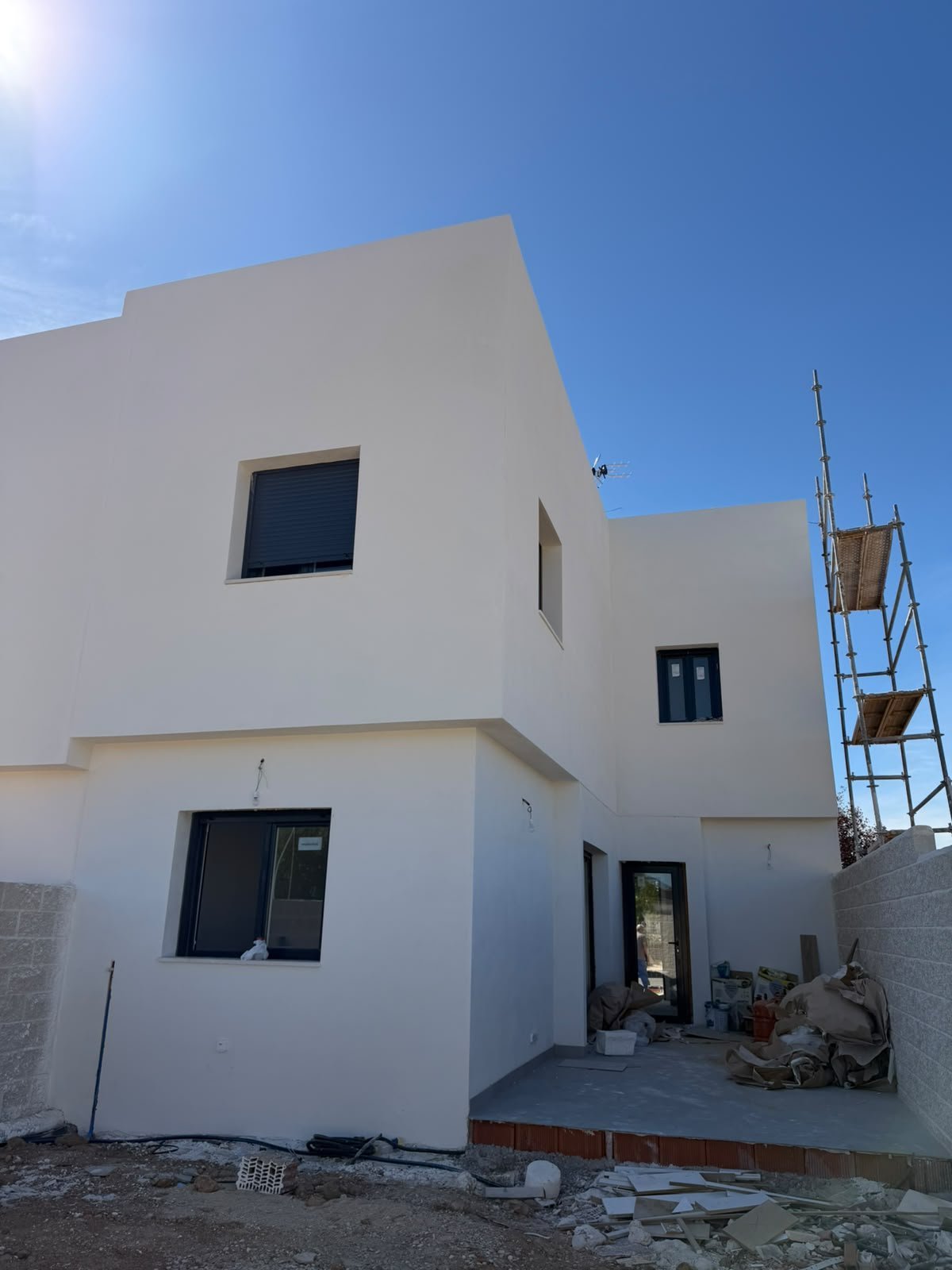 Vivienda unifamiliar de obra nueva en construcción con fachada blanca cúbica, andamios y materiales de obra bajo un cielo azul