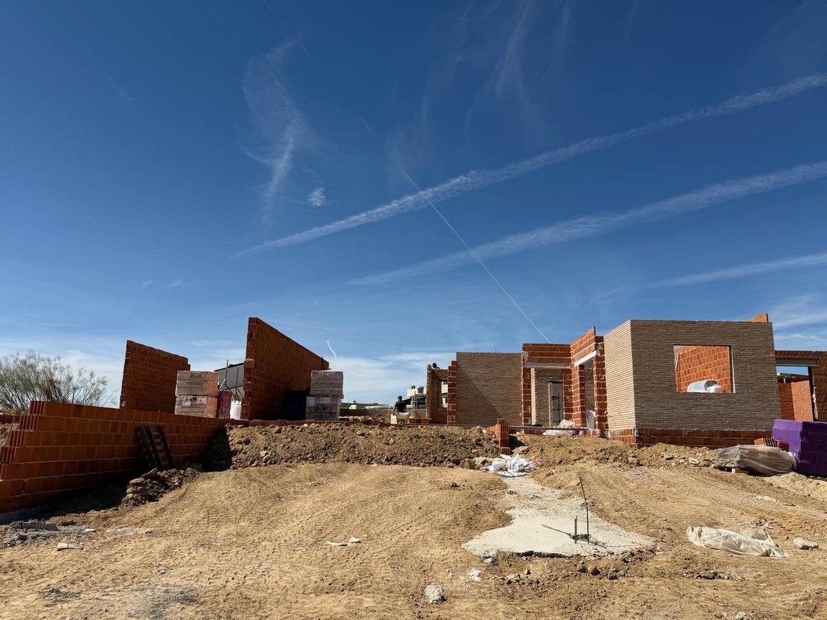 Avance de la obra de los chalets adosados de Valmojado con estructura de ladrillo y movimiento de tierras bajo cielo azul